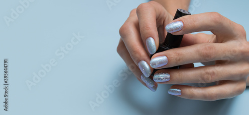 Female hands with winter manicure and a bottle of nail polish with copy space