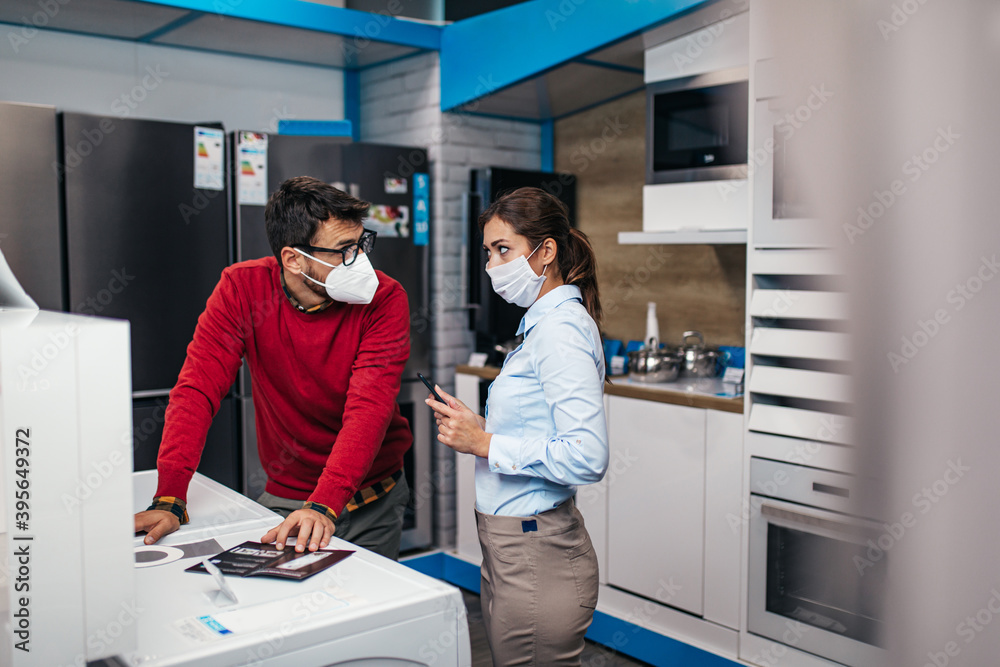 Young man talking with saleswoman in tech store. They are both with face protective masks. Pandemia, Covid-19 concept. Young man talking with saleswoman in tech store. They are both with face protective masks. Pandemia, Covid-19 concept.