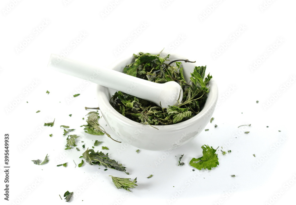 Closeup of dried nettle in a mortar with pestle, isolated on white background.