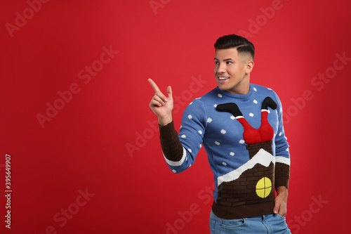 Happy man in Christmas sweater on red background, space for text © New Africa