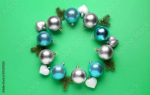 Beautiful festive wreath made of color Christmas balls and fir tree branches on green background, top view