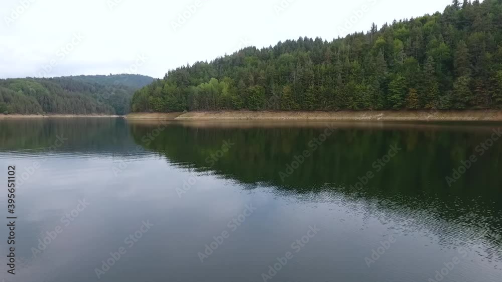 Aerial view of an outdoor place with small artificial lake on a cloudy day, located between two sides of a land surface with evergreen trees. Aerial view of an outdoor place with small artificial lake on a cloudy day, located between two sides of a land surface with evergreen trees.