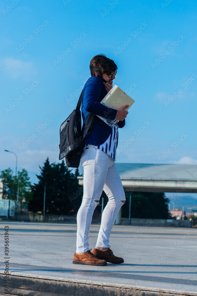 Full-length picture of a handsome young businessman standing outdoors with documents, mobile phone and briefcase.