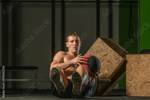 Close-up photo of a handsome bodybuilder working out seated using a medicine ball