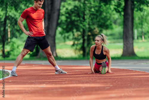 Young couple stretching before starting their morning jogging routine on a tartan track at the park.