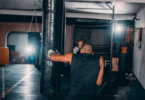 Silhouette muscular fighter training on a punching bag in the gym