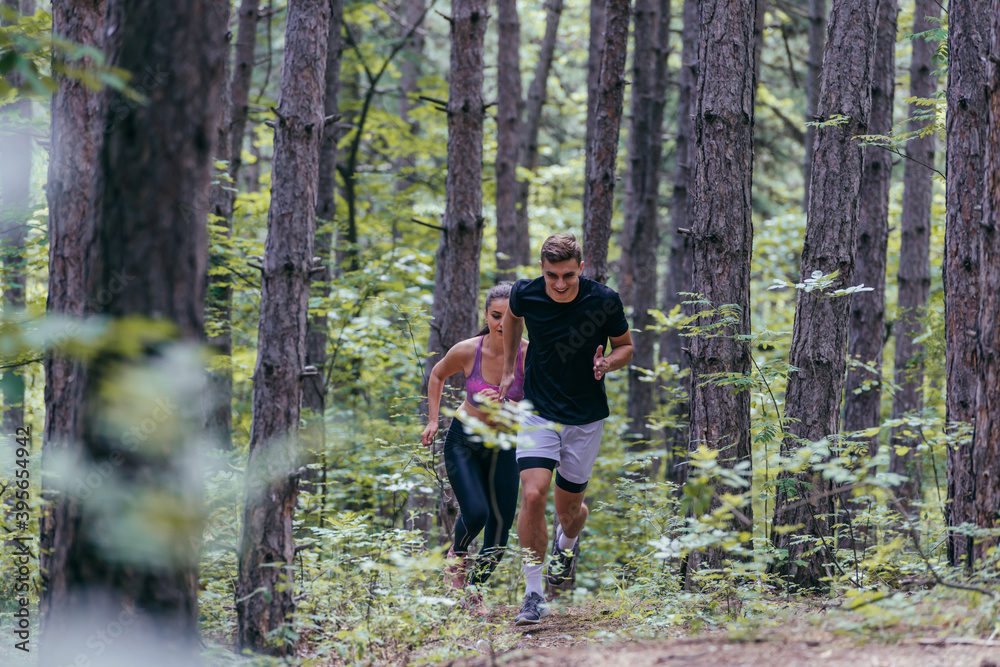 Young athletic couple is running outdoors in the wooded forest area Young athletic couple is running outdoors in the wooded forest area