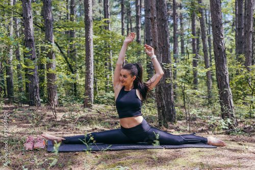 Healthy young sporty woman is making splits on a yoga mat in the forest