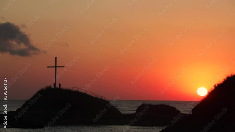 Time lapse of red sunrise in early hours in Lozenets, Bulgaria. Different shades of red are changing as the sun rises. Two people are walking around the cross on the rock, admiring the view ahead. Time lapse of red sunrise in early hours in Lozenets, Bulgaria. Different shades of red are changing as the sun rises. Two people are walking around the cross on the rock, admiring the view ahead.