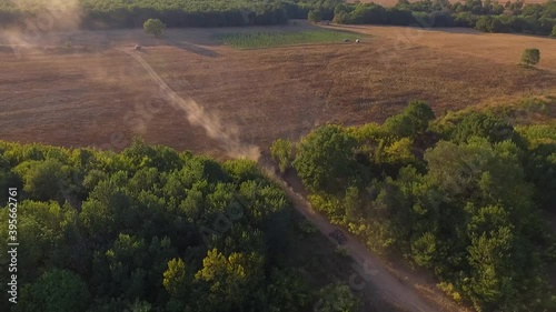 Aerial view from fast baggy which is driving with fast speed. Big clouds of dust are following from behind. Top view from drone onto race in the forest dirty road. photo