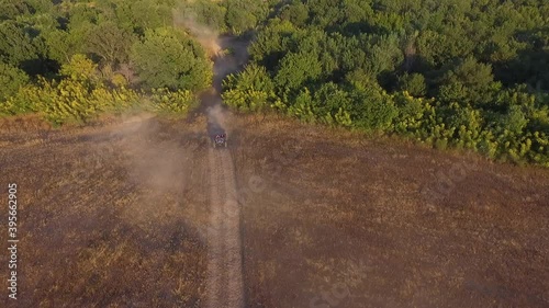 Aerial view from fast baggy which is driving with fast speed. Big clouds of dust are following from behind. Top view from drone onto race in the forest dirty road. photo