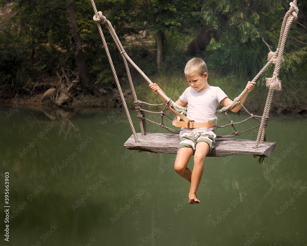 Boy swinging on a swing over the river Stock Photo
