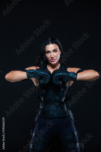 A young athletic woman in an EMS suit with Boxing gloves on an isolated black background. EMS training. Electro muscular stimulation machine. © satyrenko