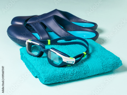 Men's swimming goggles on a towel and blue slates on a blue background.