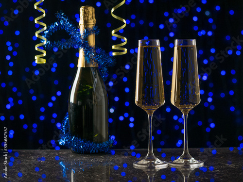 Decorated champagne bottle and two filled glasses on a blue bokeh background.