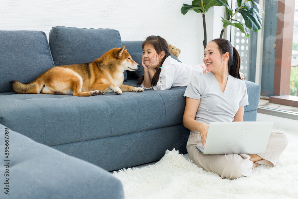 Adorable Asian mother and daughter are sitting for relaxing on the sofa with a dog.