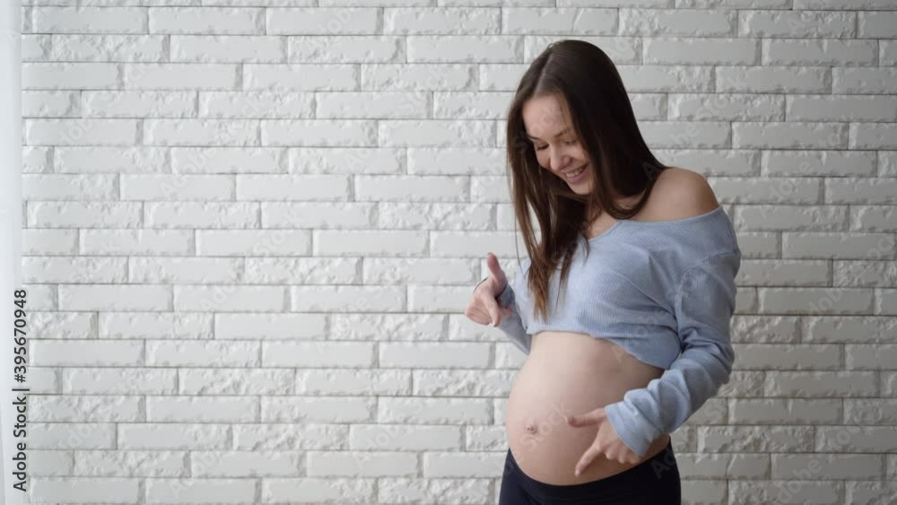a woman of European appearance stands near the wall, a smile on her face. with index fingers points to the stomach. Copy space a woman of European appearance stands near the wall, a smile on her face. with index fingers points to the stomach. Copy space