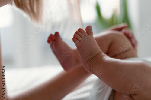 Newborn baby feet in mother's hands isolated on white. They are in the room on the bed. Motherhood concept.
