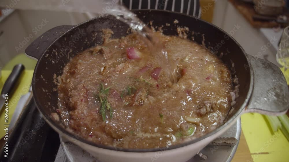 Adding water into a deep cooking pot with beef shank, onion slices, celery and spices cooked inside. Slow motion. Adding water into a deep cooking pot with beef shank, onion slices, celery and spices cooked inside. Slow motion.