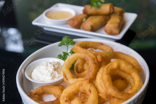 Battered onion rings with sauce tartar and vegetable spring rolls with plum sauce in the back