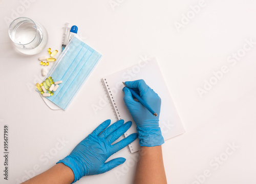 Notepad, pen, mask, pills, thermometer, syringe and glass of water on a white background. Concept of protection from diseases. The doctor writes a prescription