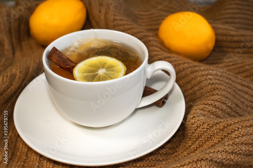 Close-up of a white Cup with tea lemon and cinnamon that stands on a warm yellow sweater on the background of blurred lemons.
