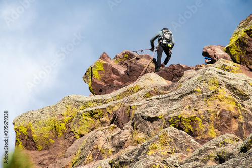 Climber repelling down from a tall multicolored rock face in Boulder Colorado. The climber is using climbing equipment to descend from one of the Flatirons