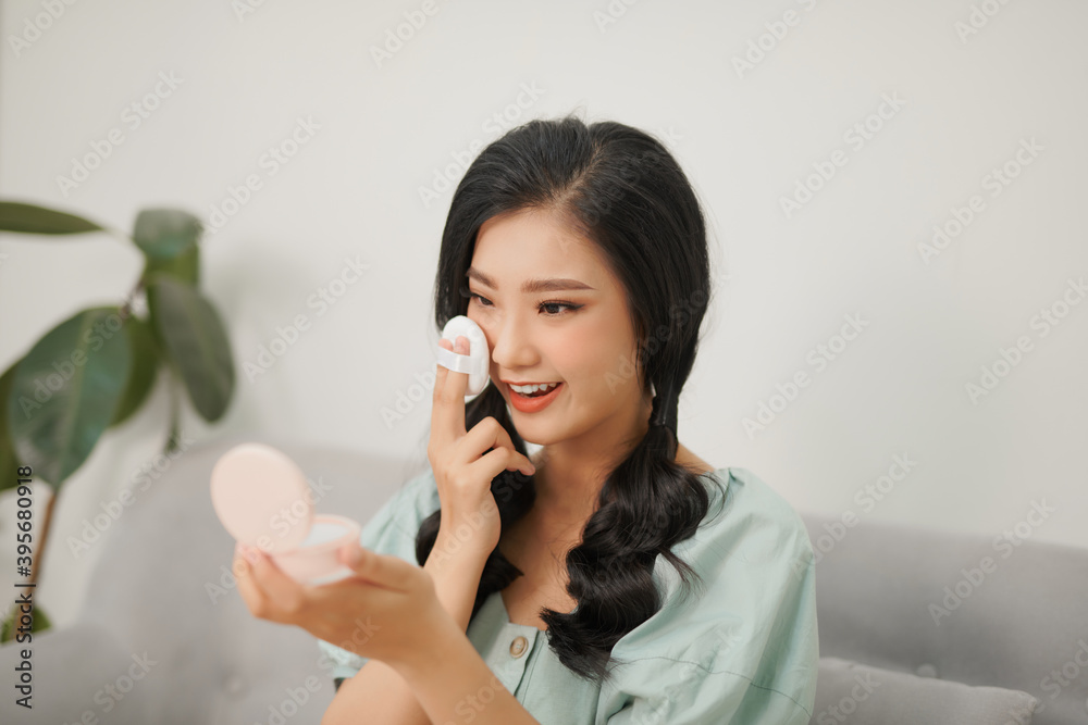 Portrait of young smiling asian woman applying cushion foundation on her face Portrait of young smiling asian woman applying cushion foundation on her face