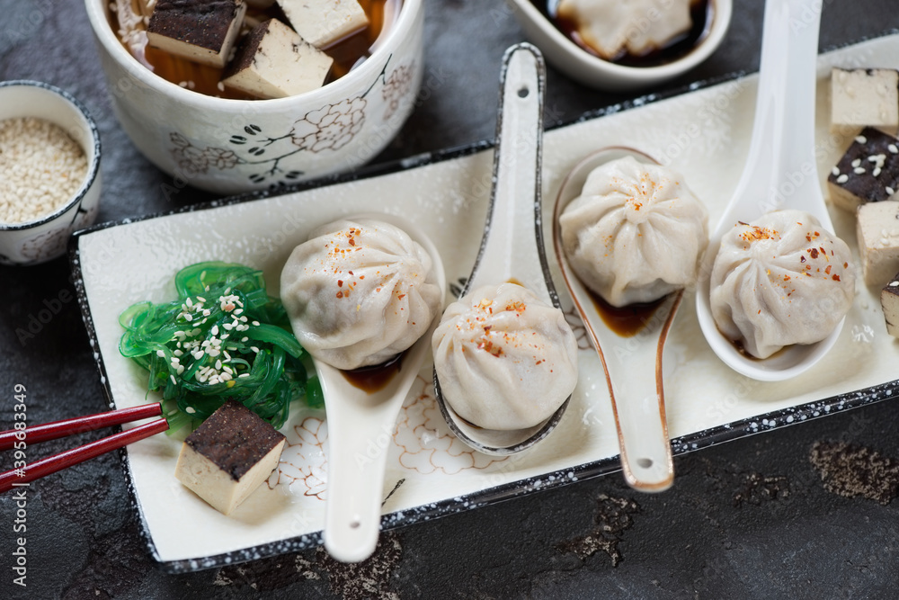 Spoons with chinese steamed soup dumplings on a white plate, elevated view on a brown stone background, closeup Spoons with chinese steamed soup dumplings on a white plate, elevated view on a brown stone background, closeup