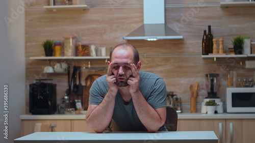 Фотография Man with headaches sitting in the kitchen massaging his temples