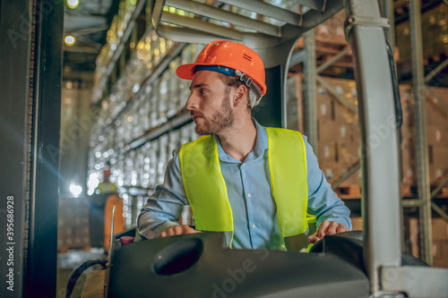 Young bearded worker in yellow vest looking concentrated