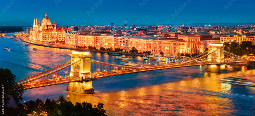 Illuminated night view of Parliament and Chain Bridge in Pest city. Panoramic evening cityscape of Budapest, Hungary, Europe. Traveling concept background..