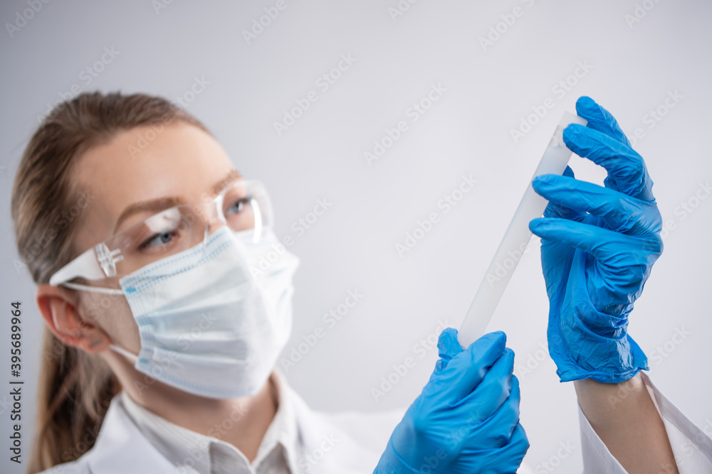 Macro shot of female doctor or laboratory assistant in protective clothing look at biological tube on white background. Research and development concept. Macro shot of female doctor or laboratory assistant in protective clothing look at biological tube on white background. Research and development concept.