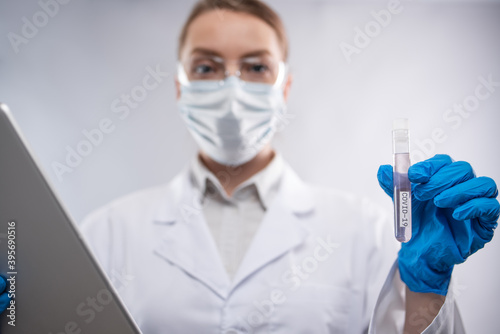 Female microbiologist in protective clothing study biological tube with covid-19 vaccine and use laptop on white background. Research and development concept. News feed.