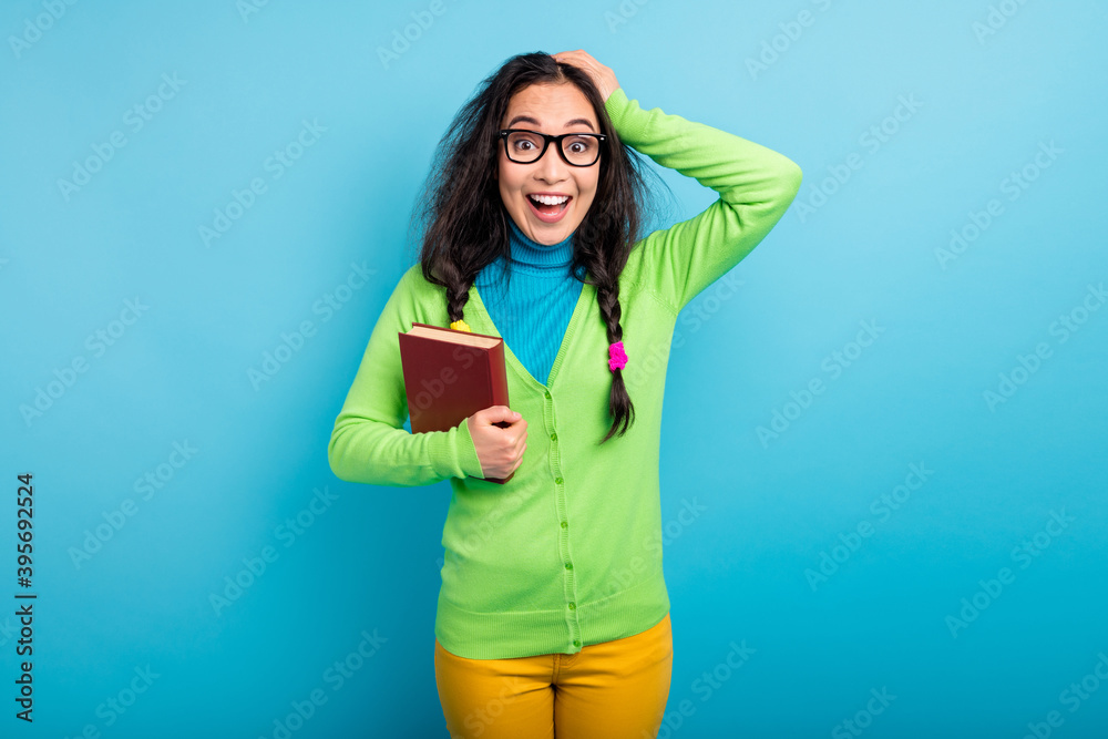 Photo of amazed charming young schoolgirl wear yellow pants hold interesting book isolated on blue color background Photo of amazed charming young schoolgirl wear yellow pants hold interesting book isolated on blue color background