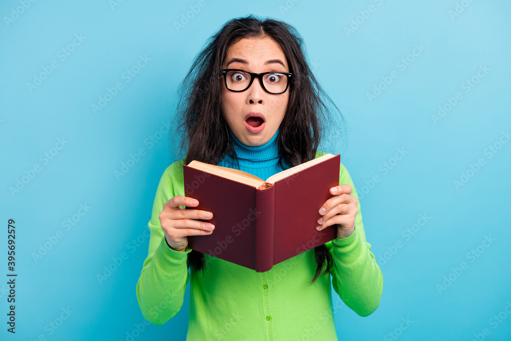 Photo of scared shocked young woman hold book wear green shirt glasses isolated on blue color background Photo of scared shocked young woman hold book wear green shirt glasses isolated on blue color background