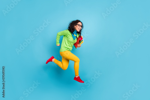 Full size profile side photo of brunette messy tails haired girl jump run empty space wear yellow pants isolated on blue color background