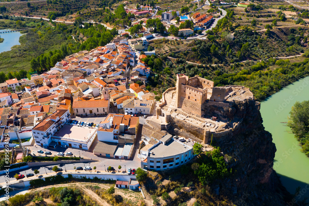 Scenic aerial view of medieval Cofrentes Castle towering over city residential buildings atop rocky cliff over Cabriel River, Valencia, Spain