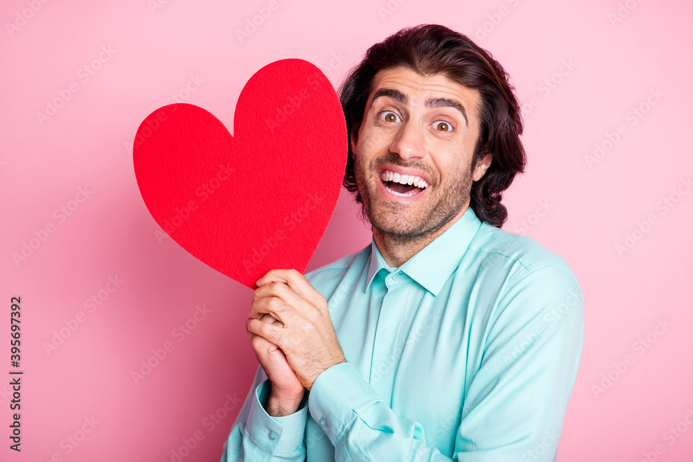Photo portrait of guy holding big red heart postcard near face isolated on pastel pink colored background Photo portrait of guy holding big red heart postcard near face isolated on pastel pink colored background