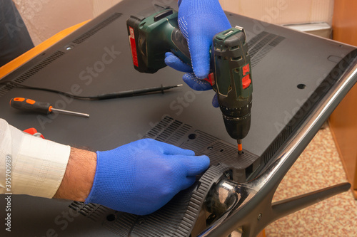 Repair of LCD TV in the service center. Engineer removes the back panel using an electric screwdriver. Selective focus, close-up.