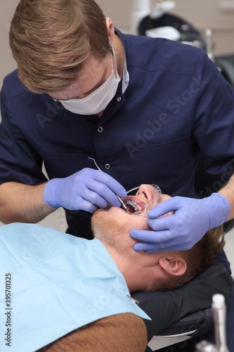 The dentist installs braces to the young man. Hands in protective gloves. Alignment of the bite or dentition. The concept of health and beauty. Vertical photo.