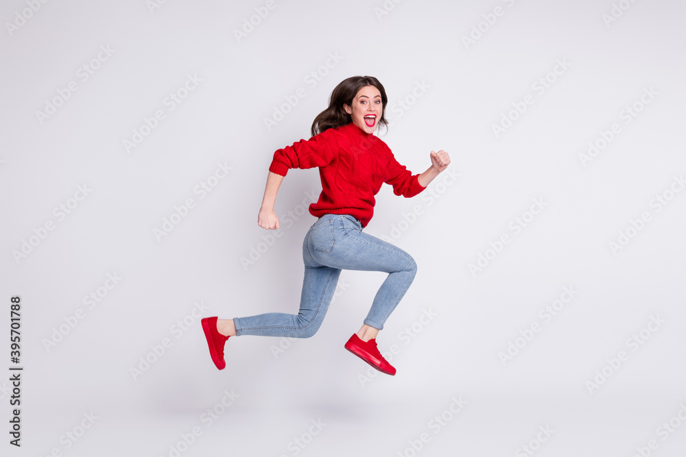 Full length body size photo of jumping running girl in jeans red sweater laughing cheerful isolated on grey pastel color background