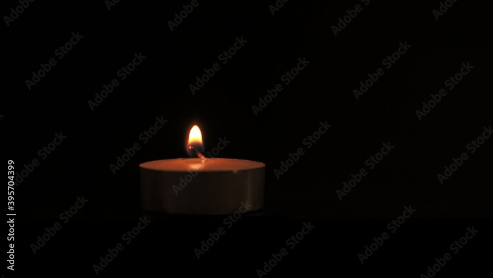 A tealight candle burning on a black background. Close-up video pannin A tealight candle burning on a black background. Close-up video pannin