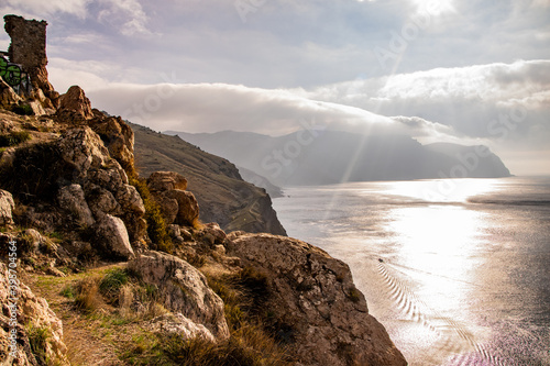 The sun peeks out from behind clouds over the sea