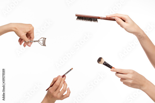 Hands with different makeup products on the white background.