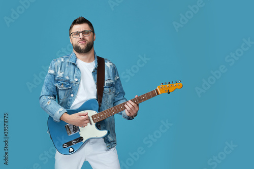 handsome man in denim with guitar isolated on blue background. copy space © producer
