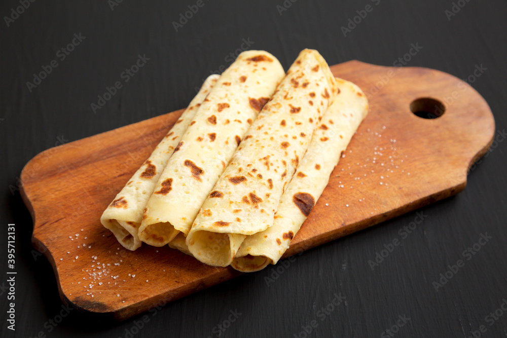 Homemade Norwegian Potato Flatbread (Lefse) with Butter and Sugar on a rustic wooden board on a black background, side view.