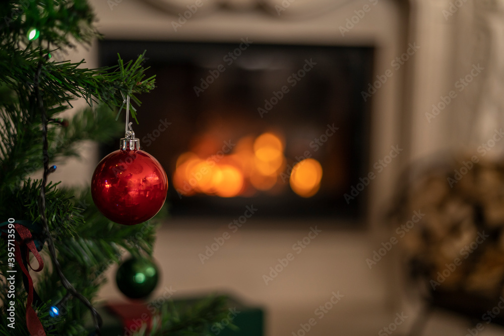 red christmas ball on a branch of christmas tree with fireplace on background red christmas ball on a branch of christmas tree with fireplace on background