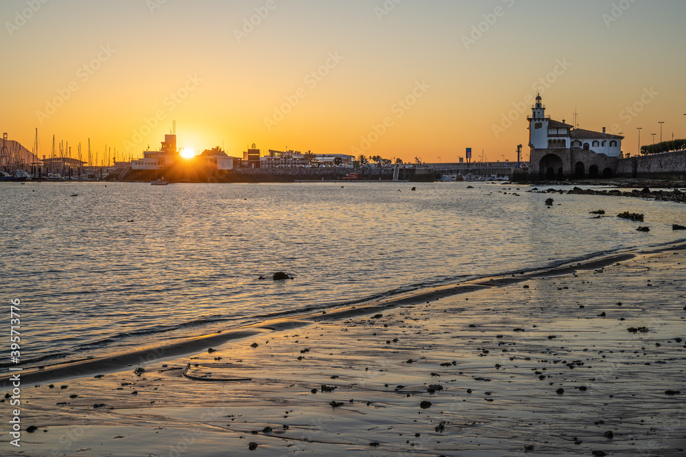 puesta de sol en la playa de la bola de getxo con rocas y faro al fondo
