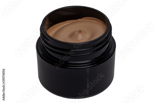Closeup of an open cosmetic jar of brown concealer cream, makeup foundation, moisturising cream for the face or an other beauty or make-up product isolated on a white background.